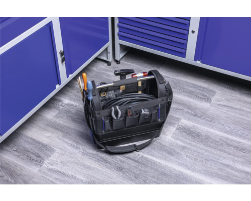 Otevřená brašna na nářadí plná nářadí před modrými dílenskými skříněmi