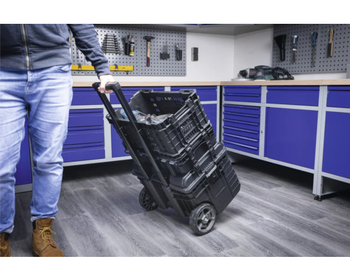 Osoba táhne vozík na nářadí s kufříky na nářadí v dílně.