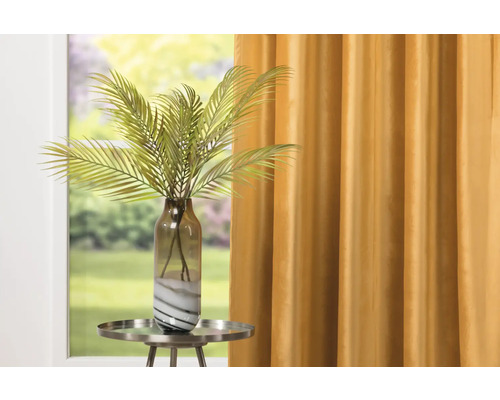 Dekorativní umělá rostlina s palmou ve skleněné váze na odkládacím stolku před závěsem