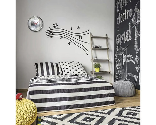 Ložnice s pruhovaným ložním prádlem, samolepkou na zeď s notami a nástěnnými hodinami se zrcadlovými koulemi