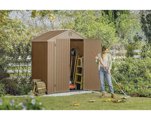 Zahradní scéna s kůlnou na nářadí, zahradním nářadím a ženou, která shrabuje listí.