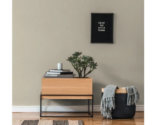 Obývací pokoj s dřevěným stolem, rostlinou, knihami, šálkem, košem s dekou a zarámovaným citátem na zdi.