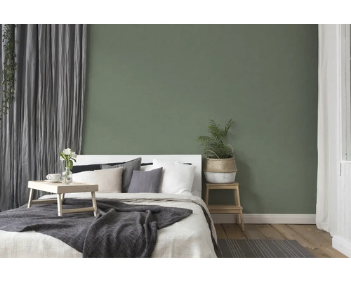 Ložnice s postelí, nočním stolkem a dekorací před zelenou stěnou