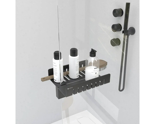 Černá sprchová police s kosmetikou a kartáčem na sprchování na sprchové stěně