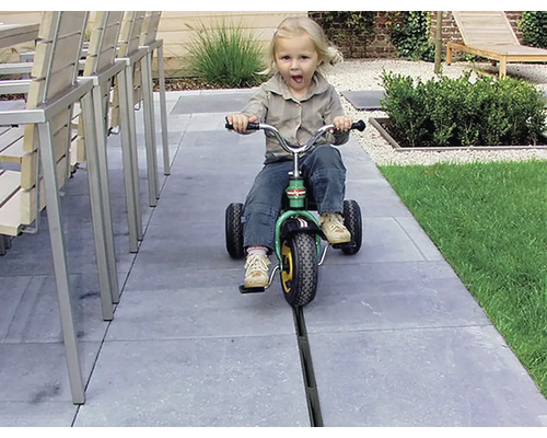 Dívka jezdí na tříkolce na terase s kamennými dlaždicemi.