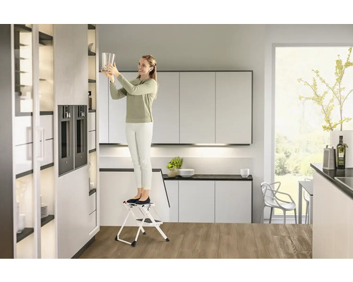 Žena na stoličce v moderní kuchyni dává sklenici do skříně