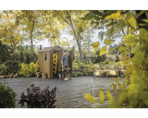 Zahradní scéna s domkem na nářadí, terasovým nábytkem a osobou s motorovou pilou.