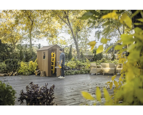 Scéna s dřevěným zahradním domkem, osobou se zastřihovačem živého plotu, žebříkem a zahradním nábytkem na terase