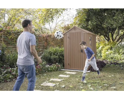 Otec a syn si hrají s fotbalem před zahradním domkem na zahradě.