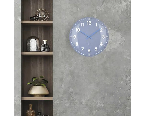 Modré nástěnné hodiny s ciferníkem visí na šedé stěně vedle dřevěné police.