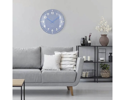 Obývací pokoj s šedou pohovkou, regálem a kulatými nástěnnými hodinami s ciferníkem