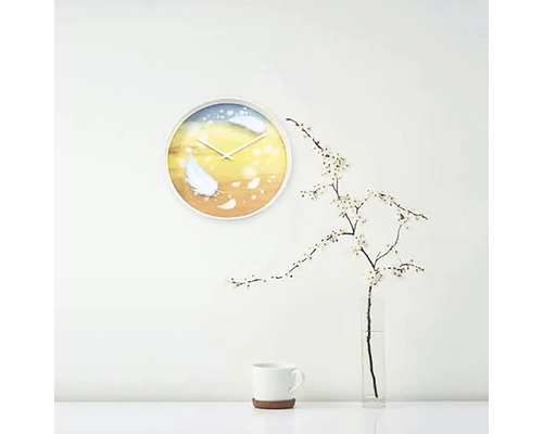 Nástěnné hodiny s motivem peří ve světlé místnosti