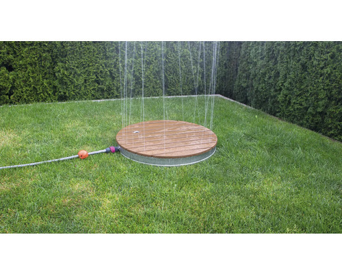 Kulatý zavlažovač trávníku ze dřeva a kovu na trávníku v zahradě.