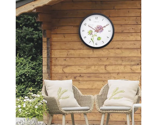 Zahradní scéna s nástěnnými hodinami na dřevěné stěně a dvěma ratanovými křesly s polštáři