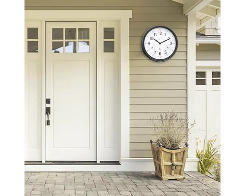 Scéna s venkovními hodinami s teploměrem na stěně domu vedle dveří a květináče.