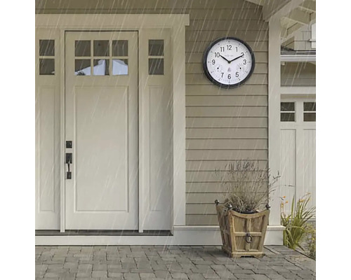 Scéna s kulatými, povětrnostním vlivům odolnými venkovními hodinami vedle vchodových dveří během dešťové přeháňky.