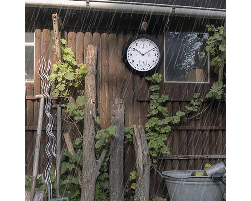 Zahradní scéna s venkovními hodinami odolnými proti povětrnostním vlivům na dřevěné stěně v dešti.
