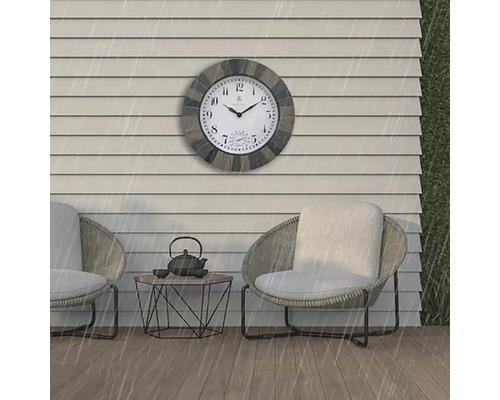 Venkovní scéna s nástěnnými hodinami odolnými proti povětrnostním vlivům nad dvěma křesly a malým stolkem