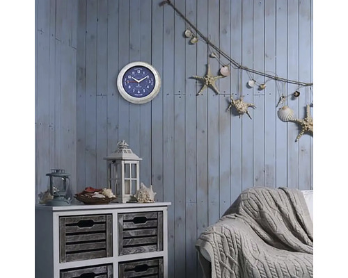 Dekorativní obývací pokoj s nástěnnými hodinami, komodou, lucernou, pohovkou a námořními dekorativními prvky, jako jsou hvězdice a mušle.