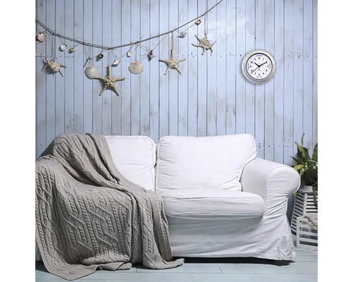 Obývací pokoj s bílou pohovkou, pletenou dekou, nástěnnou dekorací s hvězdicemi a mušlemi a nástěnnými hodinami.