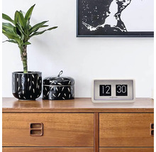 Retro hodiny s překlápěcími číslicemi na komodě s rostlinou a dózou