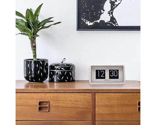 Retro hodiny s překlápěcími číslicemi na komodě s rostlinou a dózou