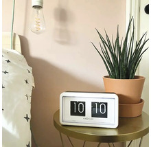 Scéna s retro překlápěcími hodinami Nextime na stole vedle postele a pokojové rostliny