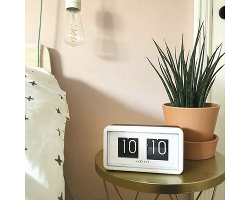Scéna s retro překlápěcími hodinami Nextime na stole vedle postele a pokojové rostliny