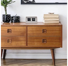 Dřevěná komoda se čtyřmi zásuvkami, na které je pokojová rostlina, dóza, překlápěcí budík a knihy