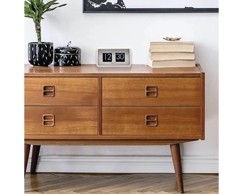 Dřevěná komoda se čtyřmi zásuvkami, na které je pokojová rostlina, dóza, překlápěcí budík a knihy