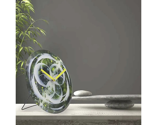 Stolní hodiny s abstraktním květinovým vzorem a žlutými ručičkami na stole