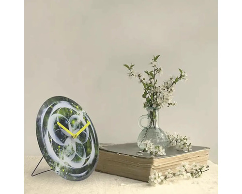 Dekorativní stolní hodiny s abstraktním designem a žlutými ručičkami vedle knihy a vázy s bílými květy.