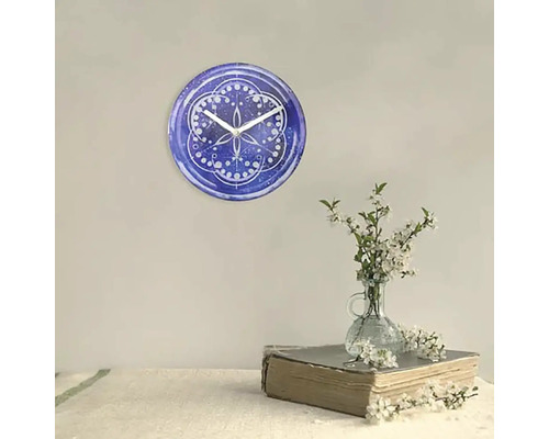 Nástěnné hodiny s modrým vzorem a bílými ručičkami vedle vázy s květinami