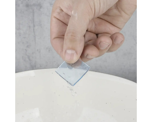 Ruka drží průhlednou lepicí podložku nad umyvadlem s vodou