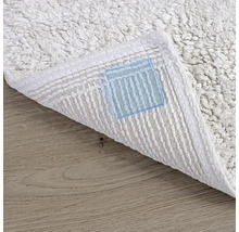 Detailní pohled na bílý koberec s viditelnou spodní stranou na dřevěné podlaze