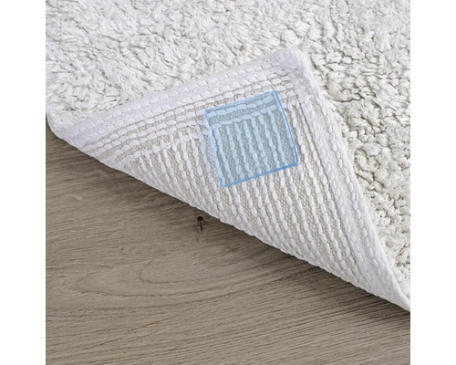 Detailní pohled na bílý koberec s viditelnou spodní stranou na dřevěné podlaze