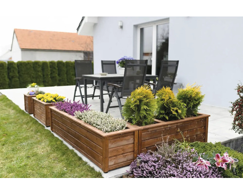 Dřevěné truhlíky s různými rostlinami na zahradě a terasový nábytek v pozadí.