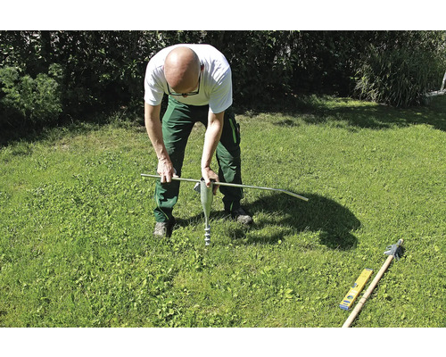 Osoba otáčí zemní kotvu tyčí v trávníku.