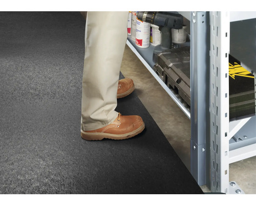 Muž stojí na gumové podložce před úložným regálem s nářadím a příslušenstvím.