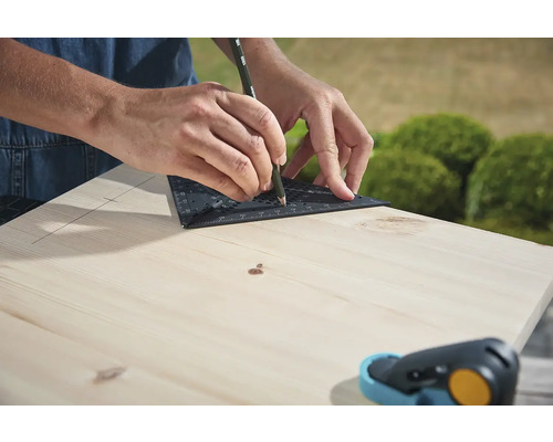 Osoba kreslí čáru pomocí úhelníku a tužky na dřevěnou desku.