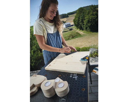 Žena rýsuje čáru na dřevěné desce pomocí úhelníku na ponku se šroubovou svěrkou a dřevěnými srdíčky
