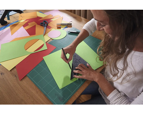 Žena kreslí zelenou papírovou šablonu pomocí trojúhelníku, podložky a tužky.