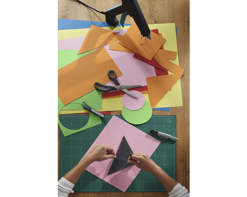 Řemeslná scéna s papírem, nůžkami, lepicí pistolí a řezací podložkou