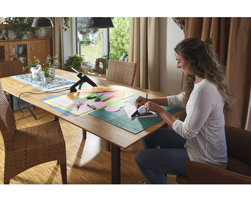 Žena vyrábí na stole s tavnou pistolí, papírem, nůžkami a podložkou na řezání