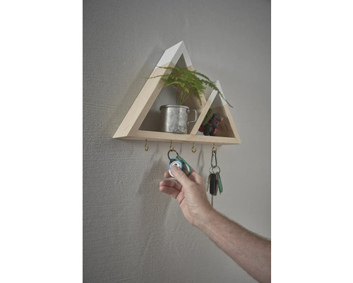 Nástěnná police ve tvaru hory s háčky na klíče a rukou, která věší klíče