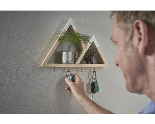 Dekorativní nástěnná police ve tvaru hory s háčky na klíče a osobou, která zavěšuje svazek klíčů