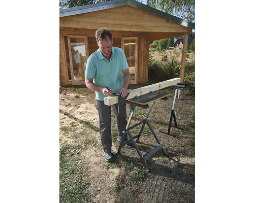 Muž kreslí čáru na dřevěné desce pomocí úhelníku a tužky na pracovním stole na zahradě.