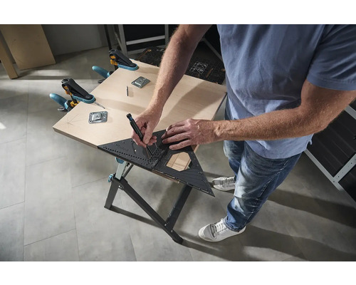 Osoba kreslí úhelníkem a tužkou na dřevěný stůl, který je upevněn svorkami.