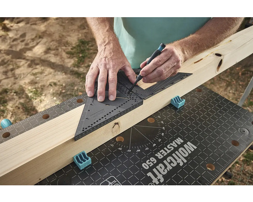 Muž používá tesařský úhelník a tužku k označení kusu dřeva na pracovním stole.