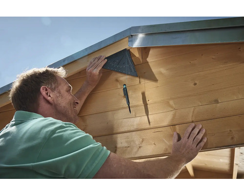 Řemeslník připevňuje úhelník k dřevěné budově.